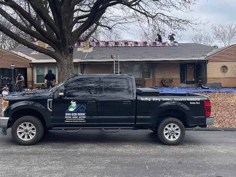 Enterprise Contracting, Inc black work pickup truck parked in front of a small residential home getting a new roof shingles installed by team members