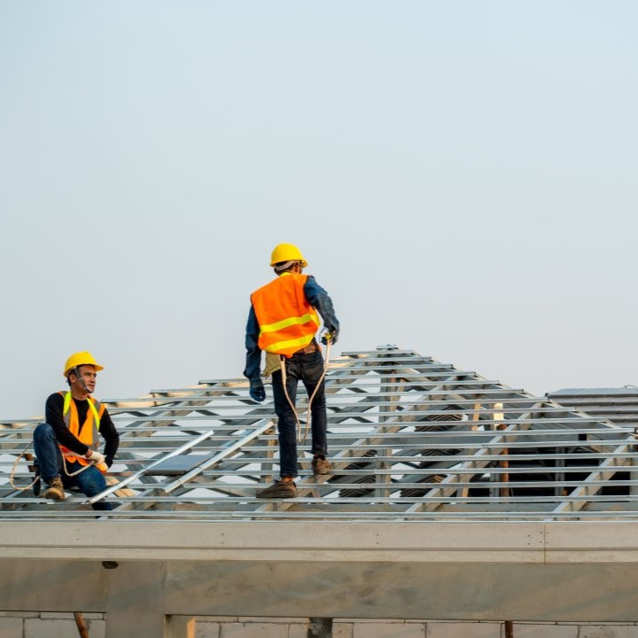 Workers with orange vests and hard hats building a metal roof frame