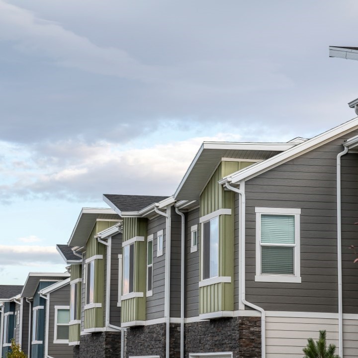 A row of properties with green and grayish colored vinyl siding