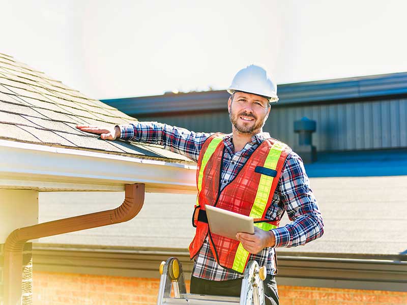 Worker with an orange vest and hard hat inspecting a residential roof